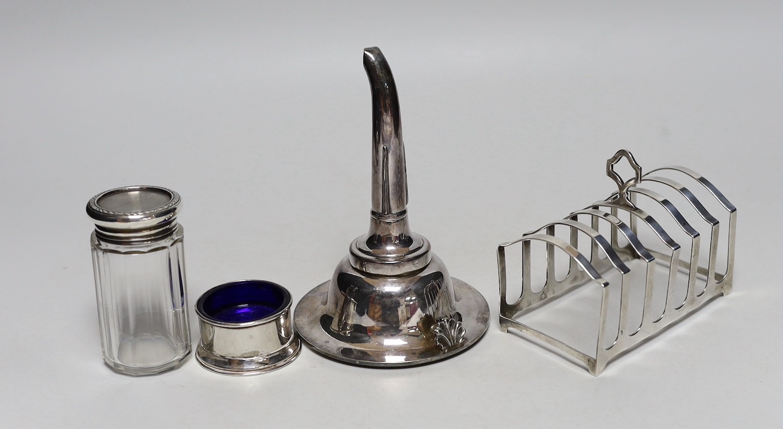 A George V silver seven bar toastrack, Birmingham, 1913, 11.9cm, four silver condiments, a silver mounted glass toilet jar and two silver plated items including a wine funnel.